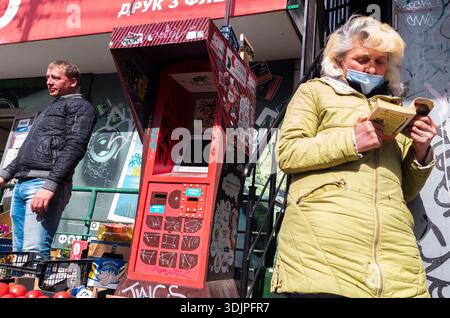 Kiew, Ukraine - 6. Mai 2023 : Frau mit Gesichtsmaske liest Buch über die belebte Kiewer Straße, Händler und Fußgänger in der Nähe im ehrlichen Stadtzentrum im Frühling Stockfoto