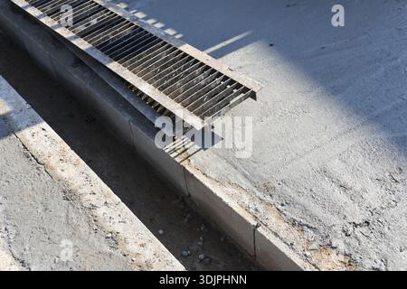 Industrieller Betonentwässerungsgraben auf der Baustelle mit robuster Metallstahlgitterabdeckung über tiefem Grabensystem zur Regenwasserbewirtschaftung Stockfoto