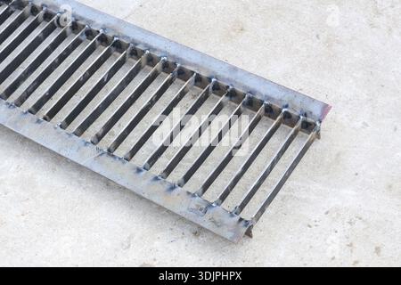 Stabiles Metallrost auf grauer Betonoberfläche, robuste Sturmabdeckung aus Stahl mit linearem Muster, Kanalgitter zum Schutz des unterirdischen Wassergrabens, sol Stockfoto