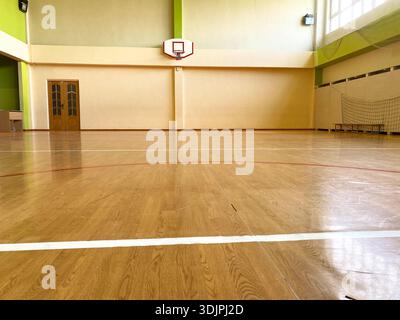 Innenraum einer Schulsporthalle mit poliertem Holzboden, Basketballkorb an der Wand und Netzbereich im Hintergrund, beleuchtet von natura Stockfoto