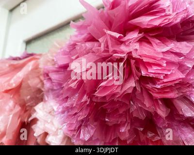 POM-Poms aus recycelten Plastiktüten in leuchtenden Rosa- und Lila-Tönen, die vor einem hellen Hintergrund angeordnet sind, ideal für eine umweltbewusste Eventdekoration Stockfoto