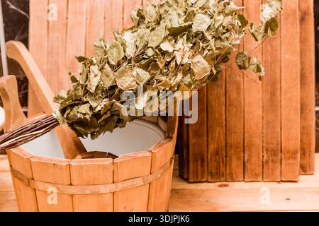 Birkenbesen am Rand eines Holzbeckens mit Wasser, umgeben von Holzpaneelen, schaffen eine traditionelle Saunaatmosphäre Stockfoto