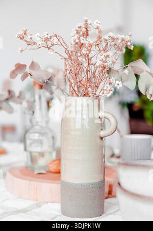 Keramikvase gefüllt mit getrockneten Blumen und Eukalyptusblättern auf einem Holztisch, die eine minimalistische Boho-Innenarchitektur-Ästhetik zeigt Stockfoto