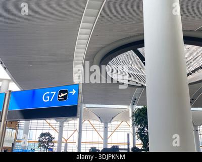 Innenansicht eines Flughafenterminals mit G7-Gate-Schild, modernem Deckendesign und dekorativen Pflanzen in einem hellen, geräumigen Bereich Stockfoto