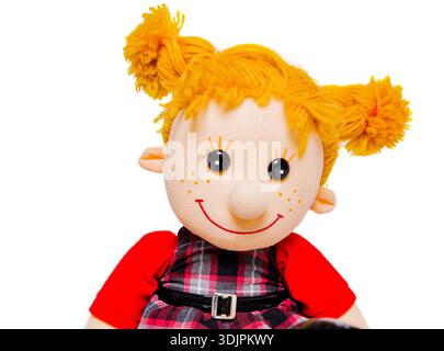 Plüschpuppe mit gelben Zöpfen und einem roten Hemd, gekleidet in einem karierten Kleid, mit einem fröhlichen Ausdruck mit großen schwarzen Augen in einer weißen Umgebung Stockfoto