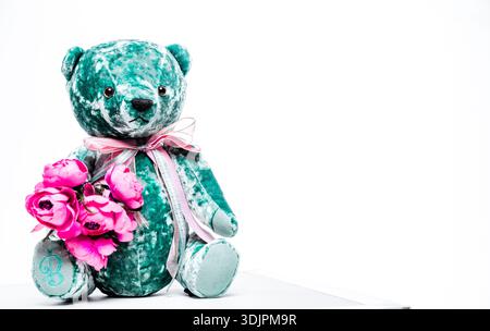 Teal Plüschteddybär mit rosafarbenen Blumen, verziert mit einem Band, auf einem sauberen weißen Hintergrund, geeignet für Kinderspielzeug und Geschenke Stockfoto