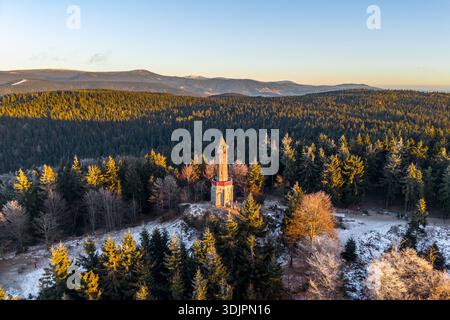 Der Stepanka-Aussichtsturm steht im Winter zwischen den Bäumen im Isergebirge. Sonnenlicht wirft Schatten über die Landschaft und erzeugt ein warmes Leuchten. Stockfoto