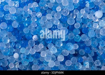 In einer Makroansicht von oben nach unten wird eine dichte Schicht kleiner, sphärischer, klarer Gelee-Granulate in verschiedenen Farben von klarem Blau und durchscheinendem weiß sichtbar. Stockfoto