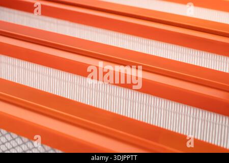 Eine Nahaufnahme mit großem Winkel erfasst mehrere parallele orangefarbene Kunststoffrahmen, die Bereiche aus weißem Faltenfiltermaterial umgrenzen Stockfoto