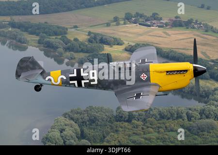 Das Foto zeigt eine Hispano HA‑1112‑M1L Buchón, eine in Spanien gebaute Variante der Messerschmitt Bf‑109, angetrieben von einem Rolls‑Royce Merlin 500‑45 V‑12-Kolbenmotor und Vierblattpropeller, die das zivile Kennzeichen G‑AWHH in Luftwaffe-Farben mit Code 9 und Seriennummer 145 auf der Veranstaltung UK Warbirds 2019 zeigt. Das Bild zeigt das Cockpitdach, die Rumpflinien und die Flügelplanform in einer Luft-Luft-Nahperspektive. Der markante Kinneinlass des Merlin-betriebenen Buchón und die historische Wollvogel-Lackierung spiegeln seine Rolle als restaurierter klassischer Flugzeugbauer wider Stockfoto