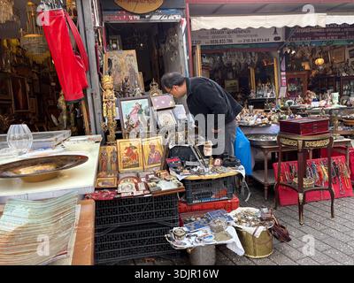Mann, der eklektische Antiquitäten und Sammlerstücke inspiziert, die auf der Straße auf dem Flohmarkt Avissinias-Platz in Athen, Griechenland, ausgestellt sind. Straßenhandel Stockfoto