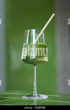 Japanische Eismatcha Latte, grüner Tee mit Milch, Sojamilch, traditionelle Matcha-Werkzeuge, mit Bambusstroh im Glas auf grünem Hintergrund. Cocktail i Stockfoto
