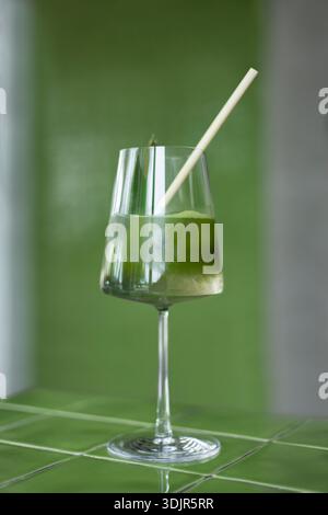 Japanische Eismatcha Latte, grüner Tee mit Milch, Sojamilch, traditionelle Matcha-Werkzeuge, mit Bambusstroh im Glas auf grünem Hintergrund. Cocktail i Stockfoto