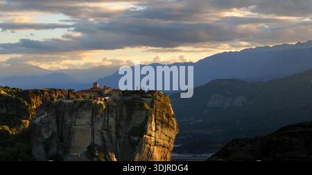 Das Kloster der Heiligen Dreifaltigkeit thront auf einem hoch aufragenden Meteora-Felsen bei Sonnenuntergang mit Bergketten, die in die Ferne verblassen, Thessalien, Griechenland Stockfoto