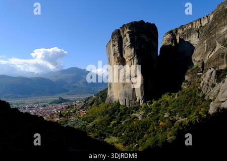 Meteora-Felsen, der sich über der Stadt Kalambaka in Thessalien erhebt, mit dramatischen Klippen, Grün und fernen Bergen unter hellem Himmel Stockfoto