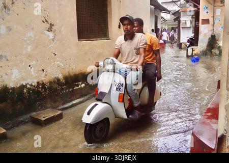 Zwei Männer fahren mit dem Roller durch die überflutete enge Gasse in Stone Town Sansibar nach starkem Regen Stockfoto