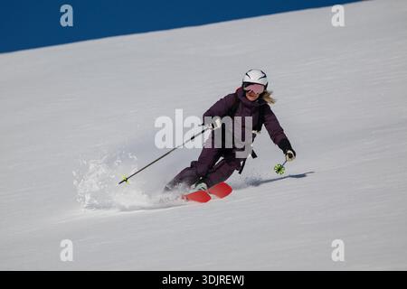 Skifahrerin, die eine Kurve auf einer verschneiten Piste macht, Helm und lila Schneeanzug trägt, im Freien Stockfoto