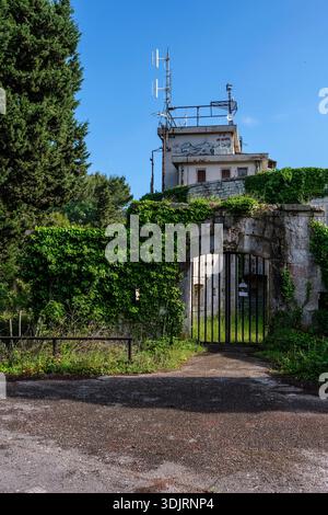 Evy-bedeckter Eingang zum Kommunikationsturm in Fort Marie Louise in Pula mit eisernem Tor, Steinmauern und Antennen unter blauem Himmel. Pula Istria Croa Stockfoto