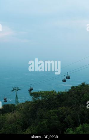 Malerische Seilbahnen, die über die üppig grünen Berghänge am Ba den Mountain in Tay Ninh, Vietnam, unter einem trüben blauen Himmel hinaufsteigen. Stockfoto