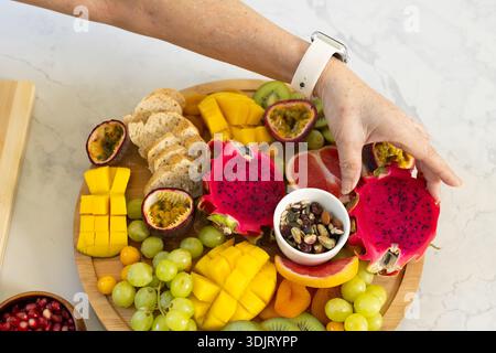 Holzplatte mit Drachenfrucht und Mango auf Marmorplatte, Unterarm mit weißer Smartwatch Stockfoto