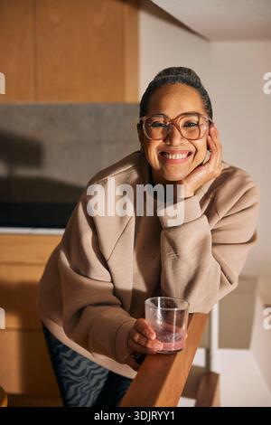 Porträt einer glücklichen, Reifen Frau, die sich auf den Ellenbogen stützt, während sie mit Saftglas in der Küche steht Stockfoto