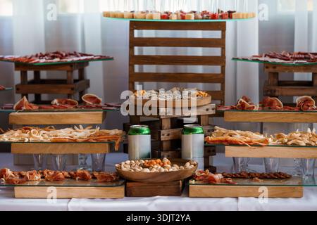 Ein wunderschön gestalteter spanischer Tapas-Aufstrich mit Wurst, Käse, Nüssen und Meeresfrüchten auf Holzständen mit Glasoberfläche, ideal für Catering Stockfoto