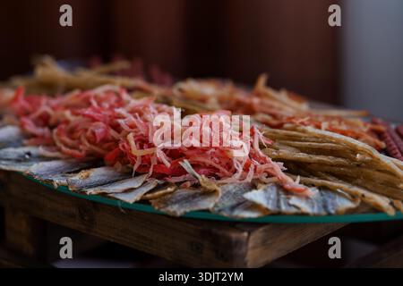 Eine rustikale Holzplatte zeigt ein appetitliches Arrangement aus dünn geschnittenem eingelegtem Gemüse und getrocknetem Fisch, das kräftige Rot- und Gelbtöne zeigt Stockfoto