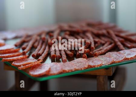 Eine wunderschön angeordnete Präsentation von Salami in Scheiben und Salami im Stilstil auf einem Serviertablett aus Glas mit satten Rottönen und marmorierten Texturen darunter Stockfoto