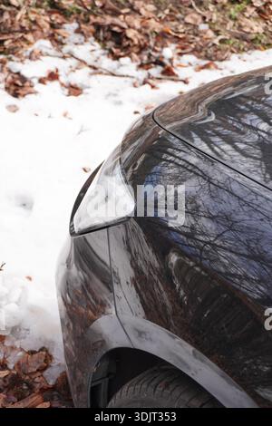 Schwarzer Autoscheinwerfer, Nahansicht, zugeschnittenes Automobilbild. Geparktes Auto. Scheinwerfer und Schnee. Winterreisen mit dem Auto. Stockfoto