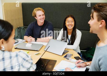 Lächelnde Studentin mit Laptop beim Gruppenstudium auf dem College-Campus Stockfoto