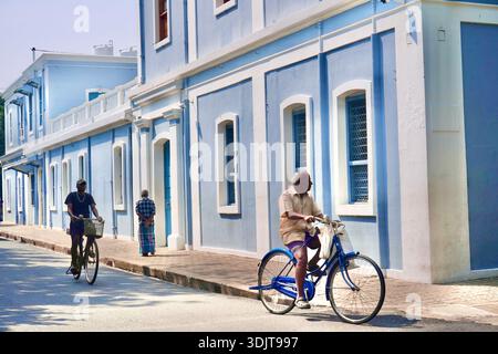 Älterer Mann radelt an pastellblauen französischen Kolonialgebäuden in Puducherry’s White Town, Indien Stockfoto