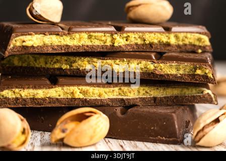Stapel Schokoladentafeln mit Pistazien-Füllung, umgeben von Nüssen auf einer rustikalen Holzoberfläche, bekannt als Dubai Chocolate. Ideal zum Nachtisch Stockfoto