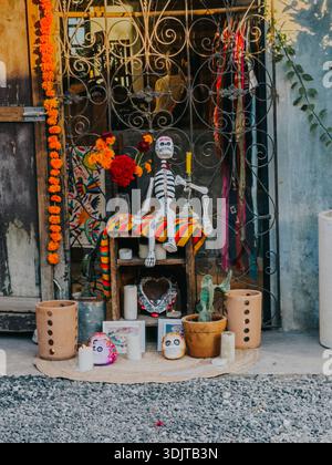 Traditioneller, vom Tag der Toten inspirierter Altar in Tulum, Mexiko, mit einer sitzenden Skelettfigur, Ringelblumen, Kerzen und Zuckerarten Stockfoto