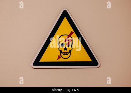 Gelbes dreieckiges Warnschild mit Schädel- und Blitzsymbol, das die Gefahr eines Stromschlags oder einer tödlichen Spannung anzeigt. Stockfoto