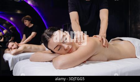Frau genießt eine Rückenmassage von einem Therapeuten in einer modernen Spa-Umgebung mit beruhigender Beleuchtung und einer ruhigen Atmosphäre Stockfoto