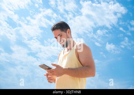 Lächelnde junge arabische und spanische Fraktionen Erwachsener am Strand mit Handy und schönem sonnigen blauen Himmel Stockfoto