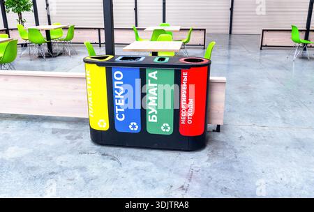 Mehrfarbige Kunststoffbehälter zur getrennten Sammlung von Abfällen. Trennen Sie Müllcontainer nach Abfallart. Text auf russisch: Kunststoff, Glas Stockfoto