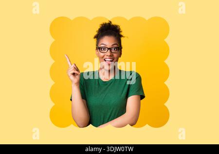 Die Person lächelt und zeigt, während sie eine Brille trägt, in einer hellen Umgebung mit gelbem Hintergrund Stockfoto