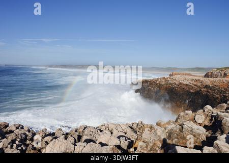 Surfen Sie mit Regenbogen an der felsigen Küste, Carrapateira, Parque Natural do Sudoeste Alentejano und Costa Vicentina, Algarve, Portugal Stockfoto