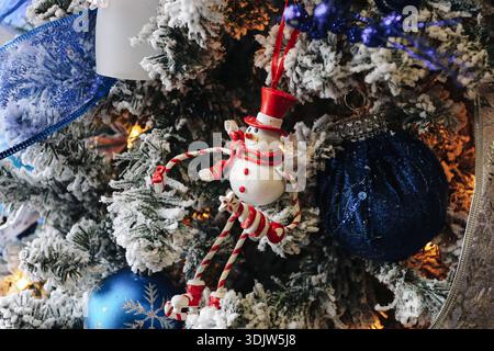 Geschmückter Weihnachtsbaum mit festlichen Ornamenten und Schneemannfigur. Winterdekoration im Innenbereich. Gemütliche saisonale Atmosphäre mit Lichtern. Stockfoto