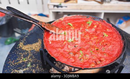 Herzhafte Tomatensoße in einer schwarzen Pfanne auf einem Grill im Freien mit frischem Basilikum Stockfoto