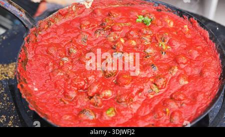Der Koch gießt Öl über Schnecken in Tomatensauce. Stockfoto