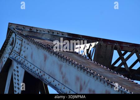 Nahaufnahme von Eisenbahnbrücken, durch Zoomobjektiv gesehen, vom Boden vor klarem blauem Himmel. Rivots halten diesen Teil der Brücke zusammen Stockfoto