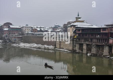 Ein Bootsmann rudert nach frischem Schneefall in der Altstadt von Srinagar, der Sommerhauptstadt von Jammu und Kaschmir, mit seinem Boot über den Fluss Jhelum. Stockfoto