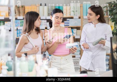 Aufmerksame Käufer von Mutter und Tochter scannen qr-Code für eine Schachtel mit Salbe oder Gel in der Apotheke, Apothekerin hilft bei der Auswahl und dem Angebot Stockfoto