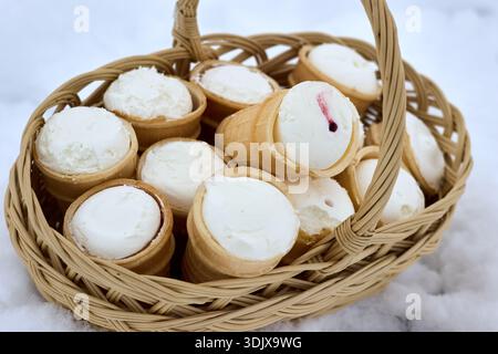 Dieses Bild zeigt einen bezaubernden Korb mit Waffelbechern, gefüllt mit cremigem, weißem Vanilleeis. Die Szene spielt draußen, mit Th Stockfoto