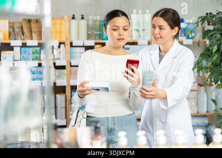 Frau, die Salbe scannt, während der Apotheker freundliche Unterstützung anbietet Stockfoto