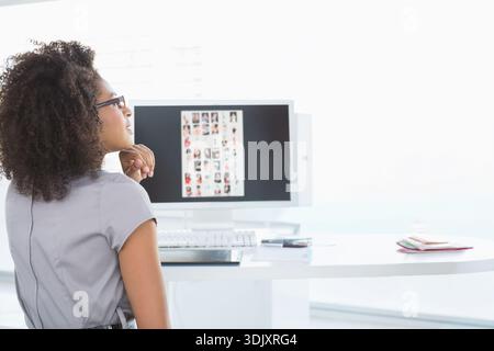 Der helle Arbeitsbereich zeigt einen Monitor mit Miniaturansichten, Tastatur, Smartphone und Notebooks auf dem Schreibtisch. Professionell, Designer, Brille, minimalistisch, sonnenbeleuchtet, stu Stockfoto