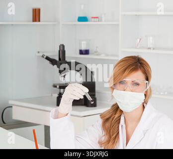 Das durchsichtige Reagenzglas mit rosa-violetten Flüssigkeiten befindet sich auf dem Labortisch in der Nähe von Mikroskop und Pipette. Wissenschaftler, Forscher, Labor, steril, klinisch, Stockfoto