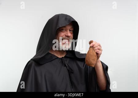 Ein alter Mönch in einem schwarzen Gewand mit einer Tüte Geld auf weißem Hintergrund Stockfoto